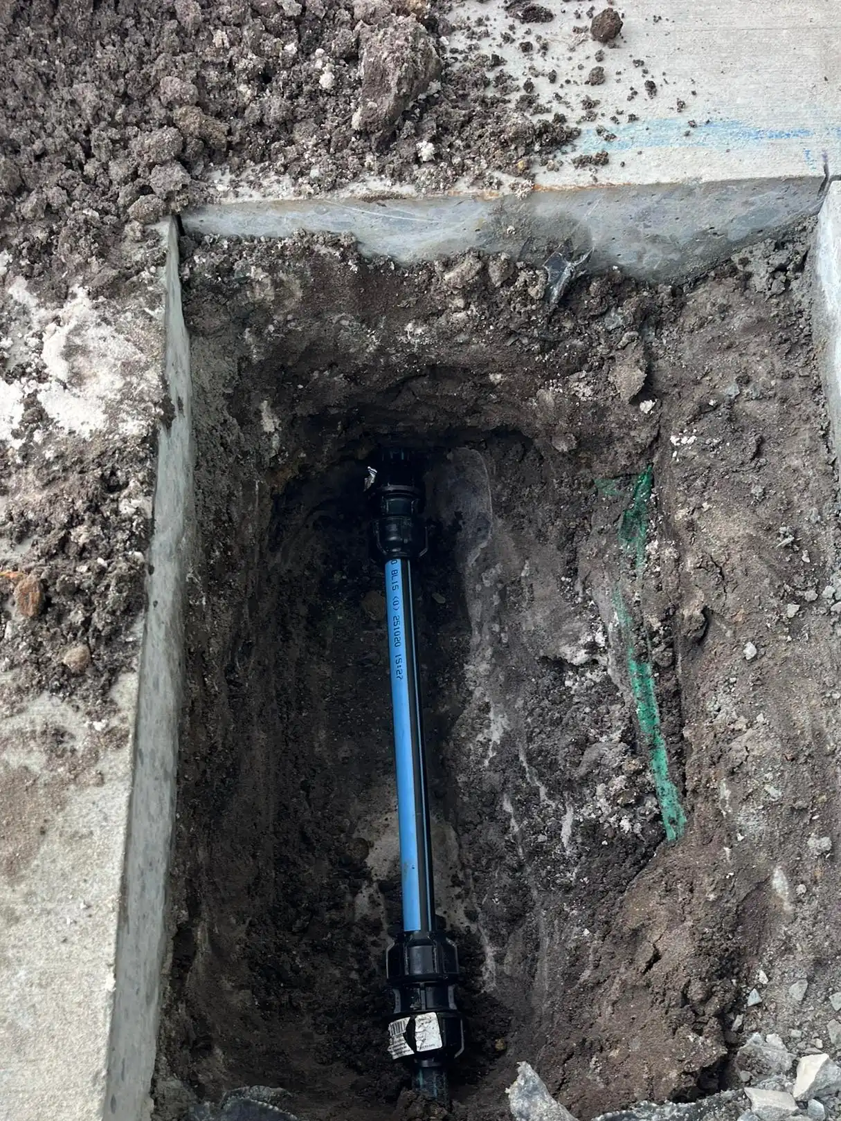 A new section of blue poly pipe joined with black compression fittings, laid in a cut-out in a concrete slab.