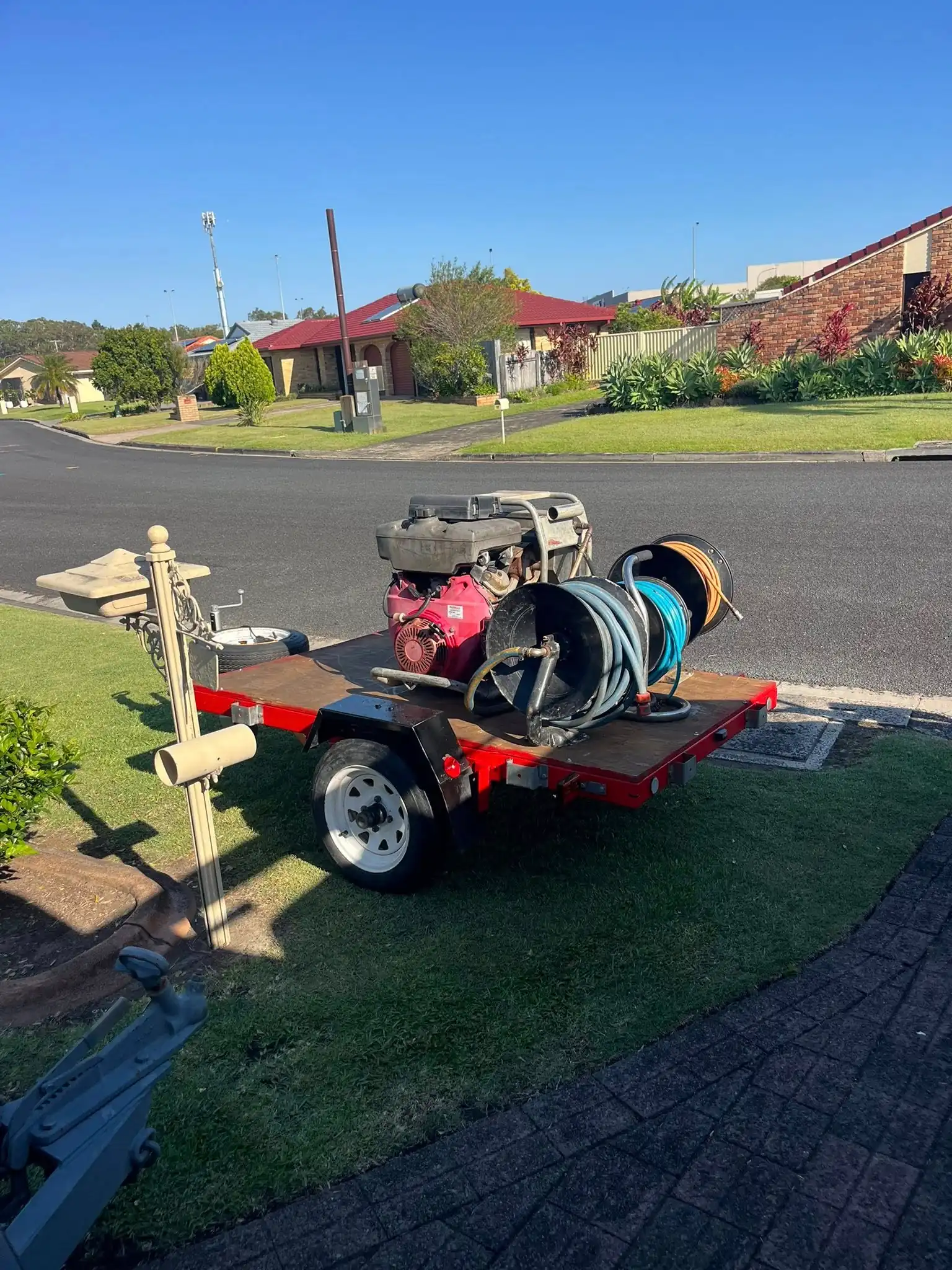A trailer carrying a petrol-powered high-pressure water jetter and two hose reels, parked on a lawn.
