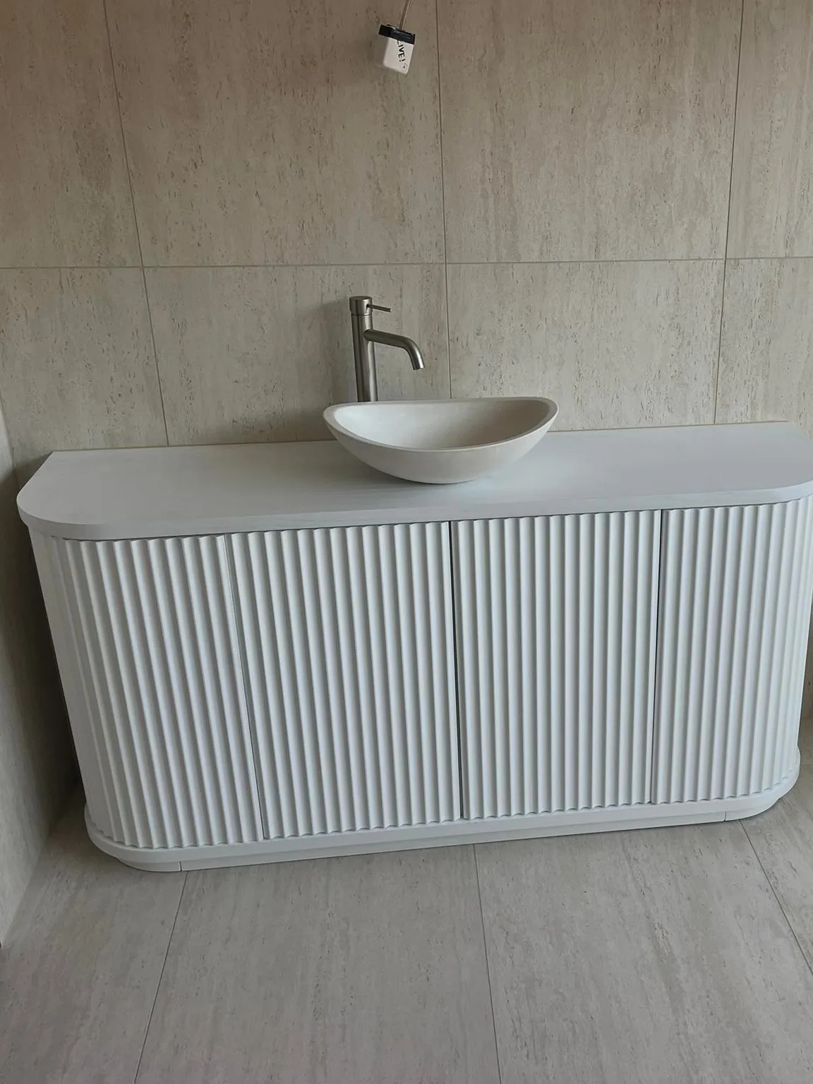 A white fluted vanity with a stone basin and a tall brushed-steel mixer tap on a tiled wall.